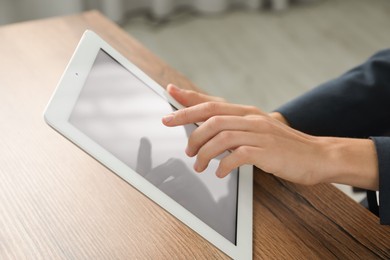 Photo of Businesswoman using tablet at wooden table indoors, closeup. Modern technology