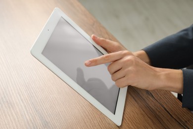 Photo of Businesswoman using tablet at wooden table indoors, closeup. Modern technology