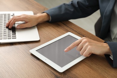 Photo of Businesswoman using laptop and tablet at wooden table indoors, closeup. Modern technology