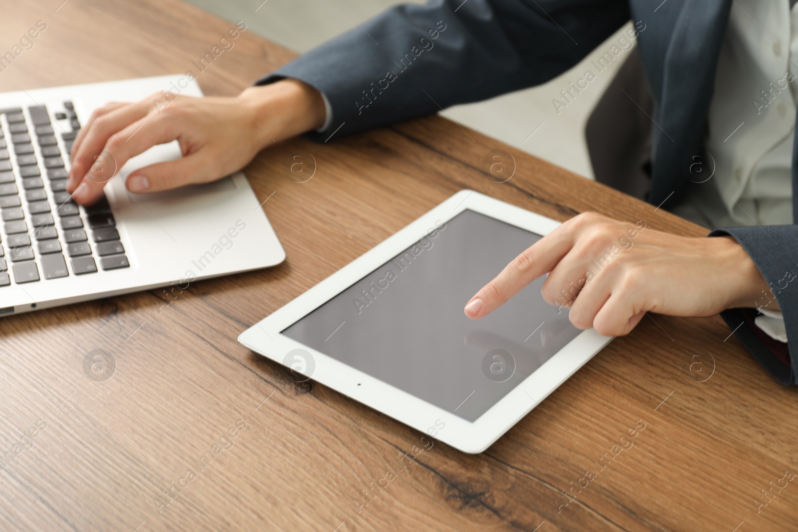 Photo of Businesswoman using laptop and tablet at wooden table indoors, closeup. Modern technology