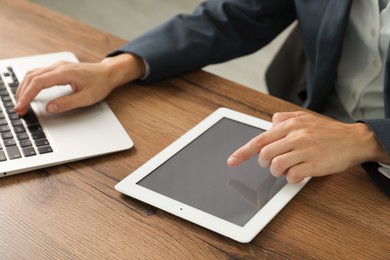 Photo of Businesswoman using laptop and tablet at wooden table indoors, closeup. Modern technology