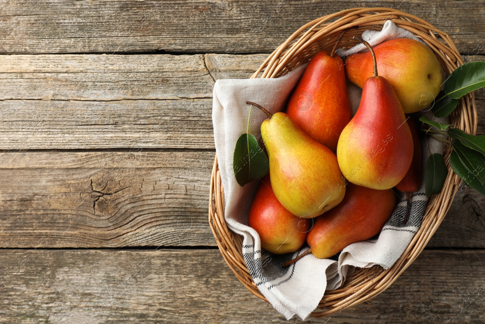 Photo of Ripe juicy pears in wicker basket on wooden table, top view. Space for text