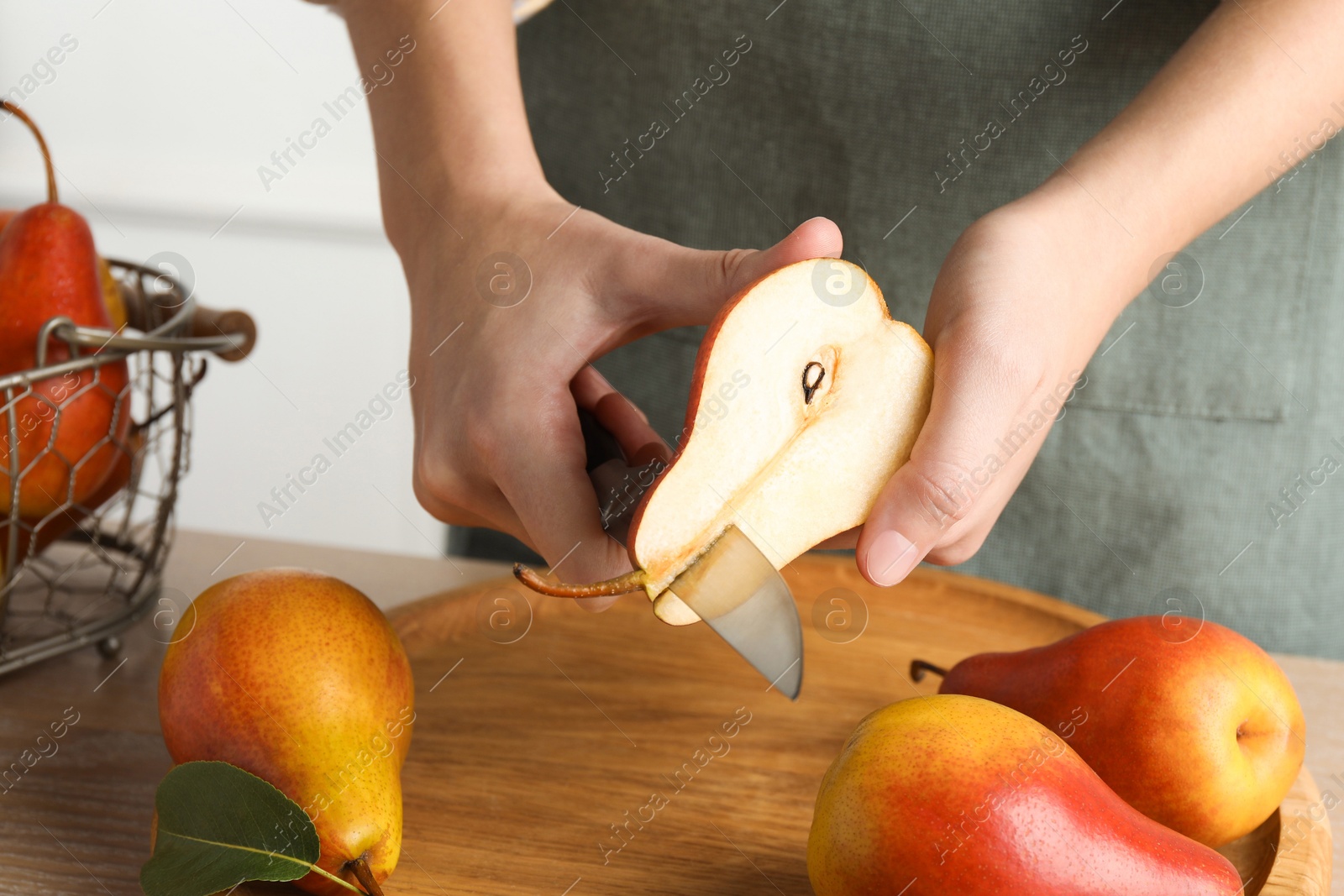 Photo of Woman cutting ripe juicy pear at table, closeup