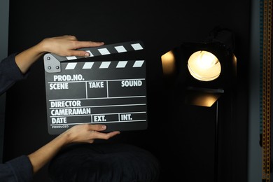 Photo of Woman with clapperboard near spotlight on black background, closeup