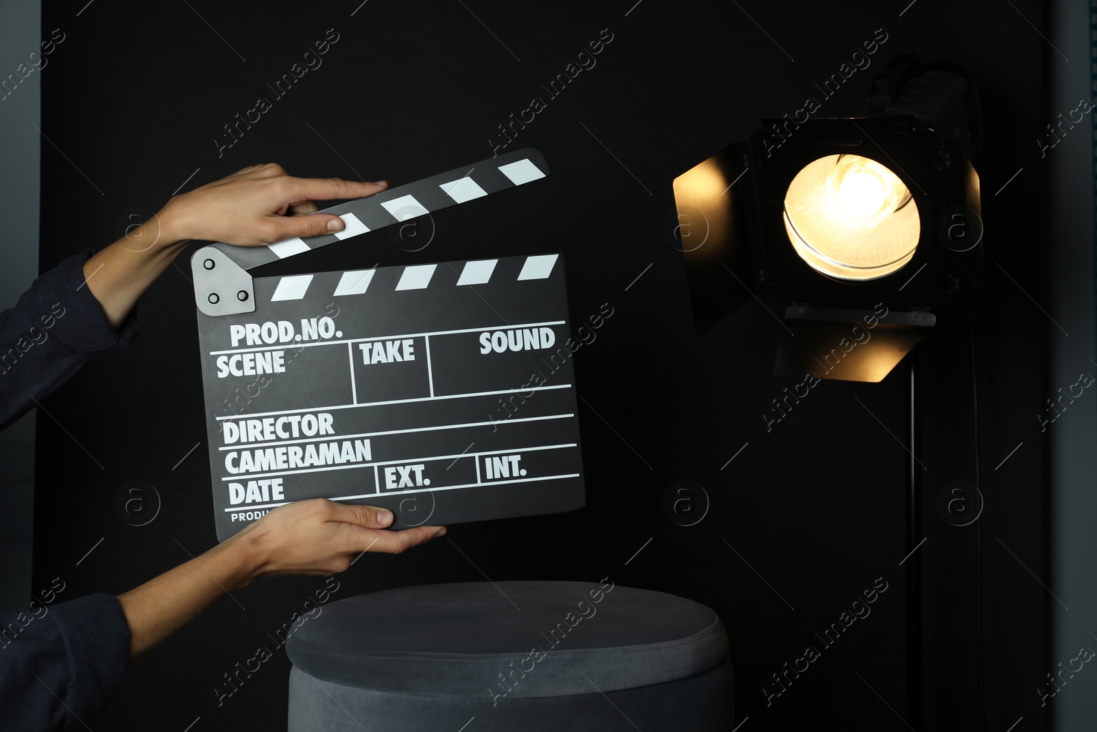 Photo of Woman with clapperboard near spotlight on black background, closeup