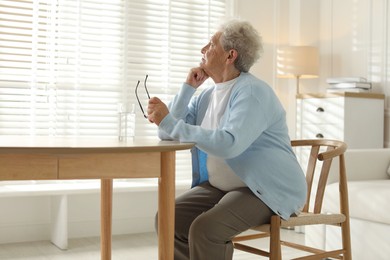 Photo of Lonely senior woman looking out window at table with glass of water indoors