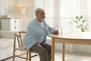 Photo of Thoughtful senior woman feeling lonely at table with glass of water indoors