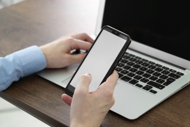 Photo of Businessman using smartphone near laptop at wooden table indoors, closeup. Modern technology