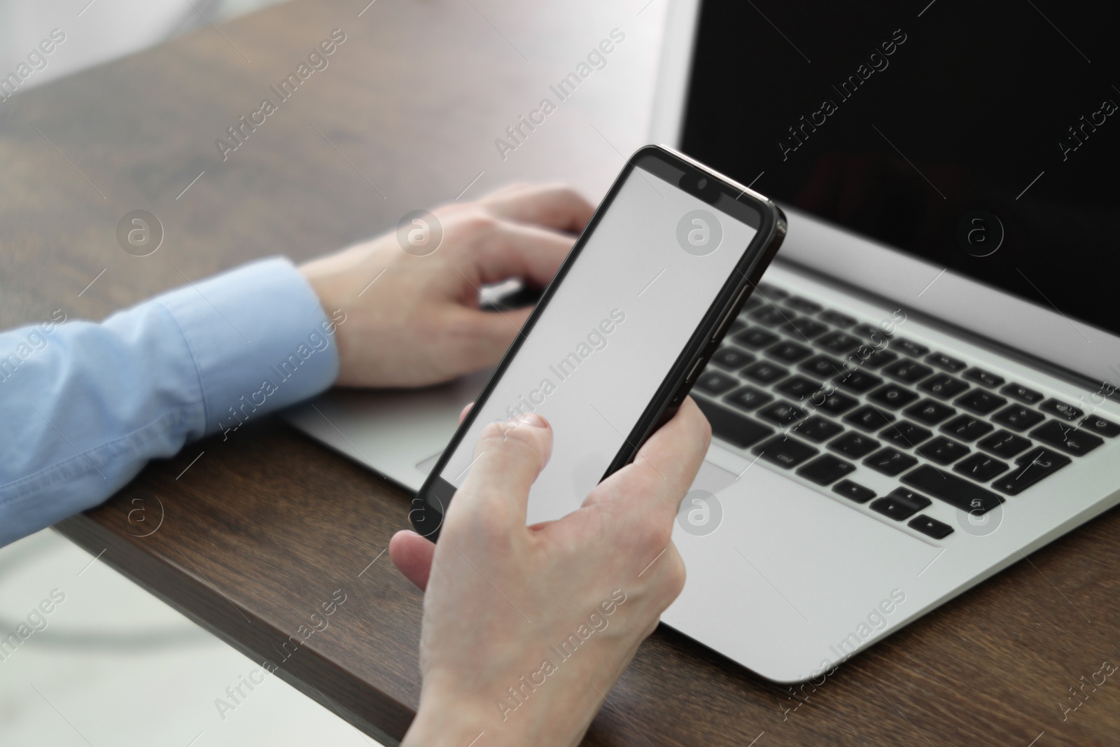 Photo of Businessman using smartphone near laptop at wooden table indoors, closeup. Modern technology