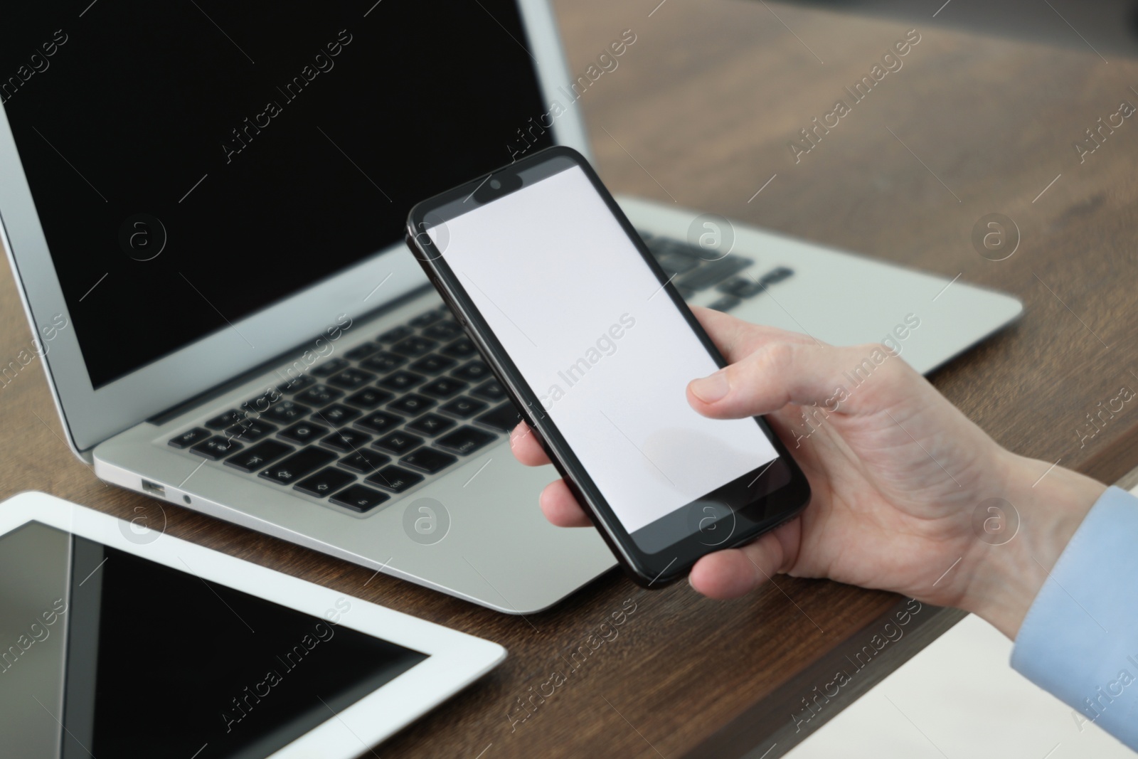 Photo of Businessman using smartphone near laptop and tablet at wooden table indoors, closeup. Modern technology