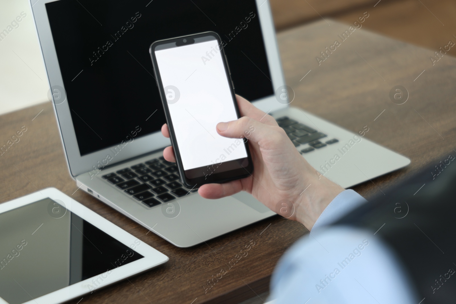 Photo of Businessman using smartphone near laptop and tablet at wooden table indoors, closeup. Modern technology