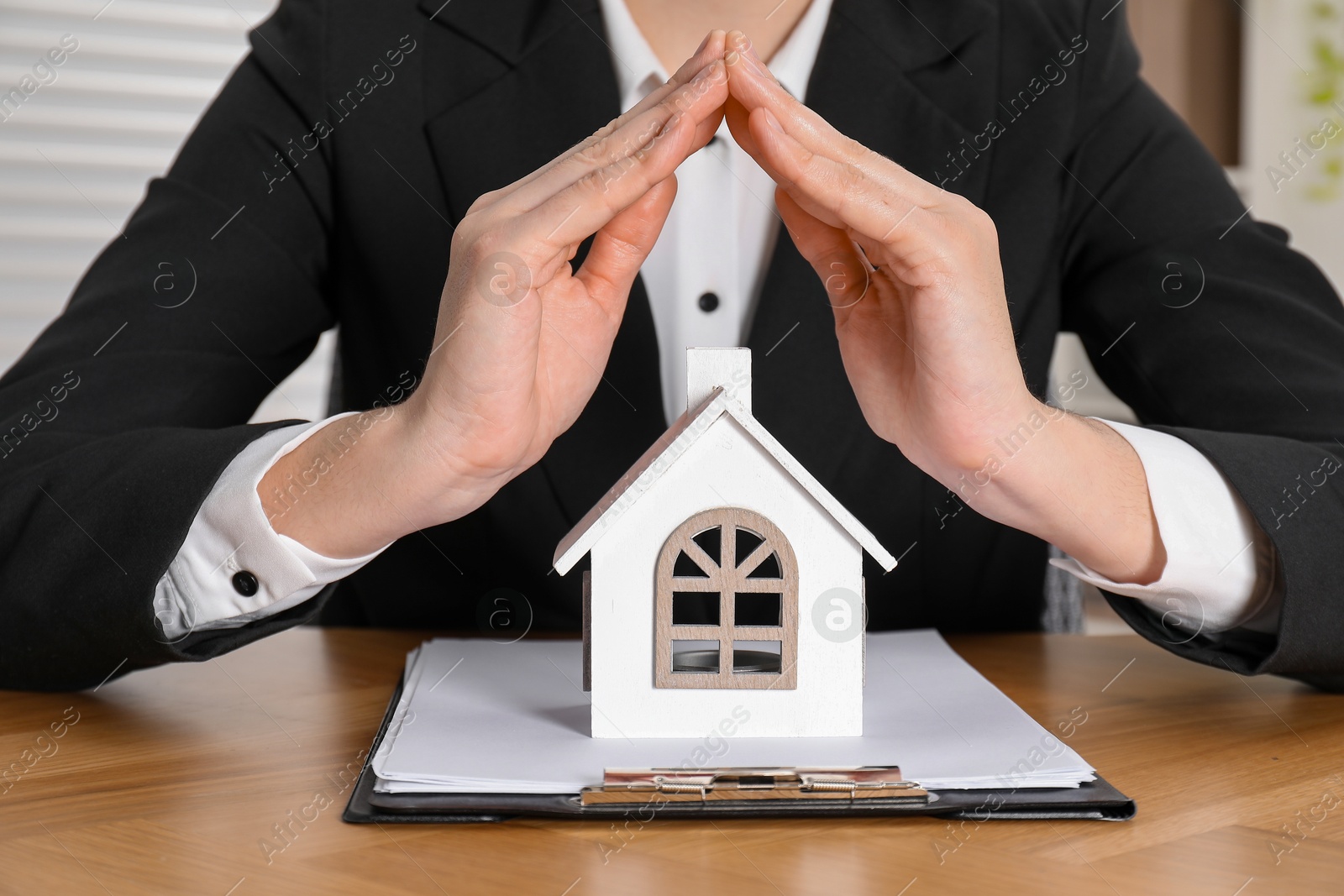 Photo of Property insurance. Real estate agent protecting house figure at wooden table indoors, closeup