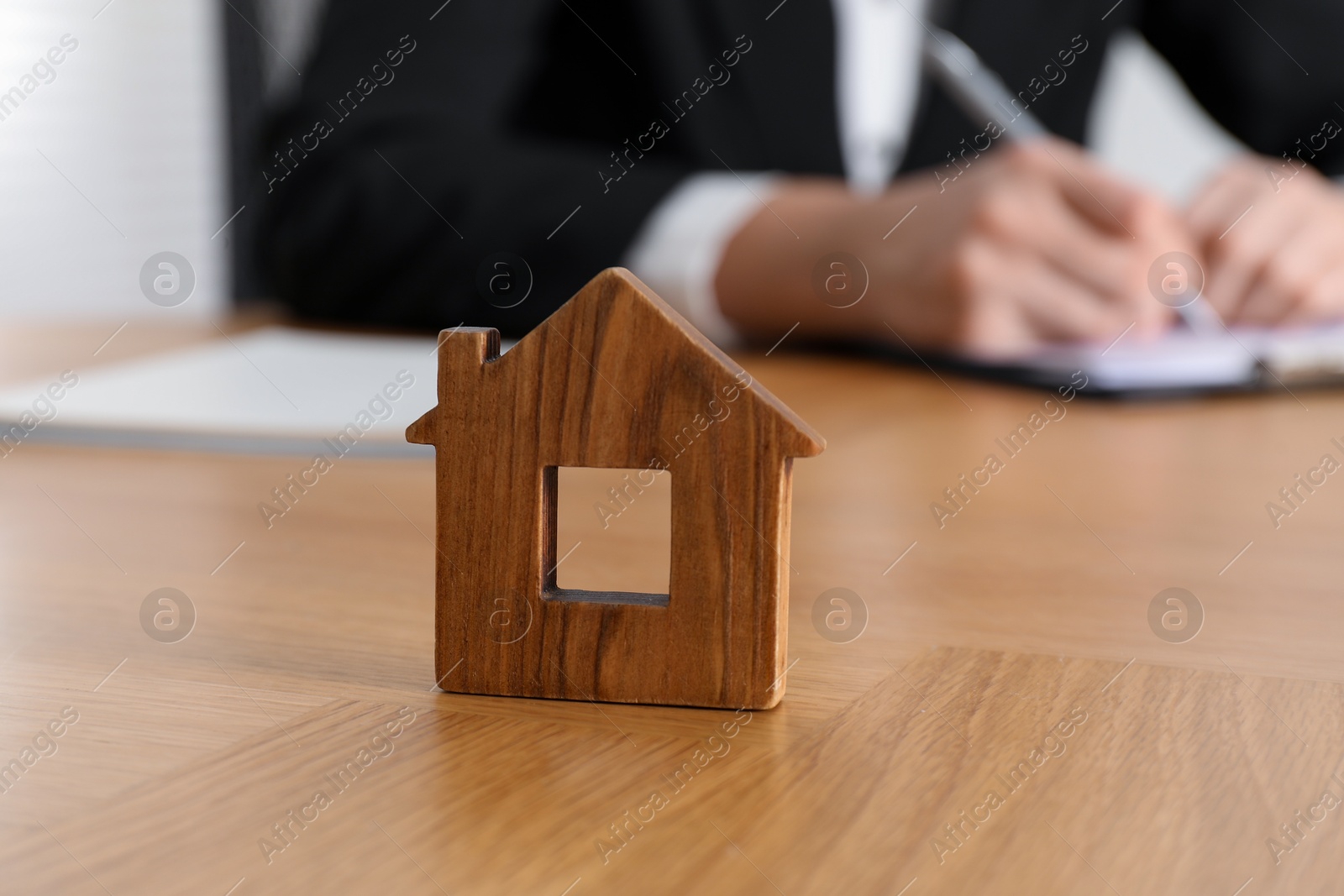 Photo of Property insurance. Real estate agent working at table indoors, focus on wooden house figure