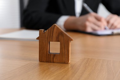 Photo of Property insurance. Real estate agent working at table indoors, focus on wooden house figure