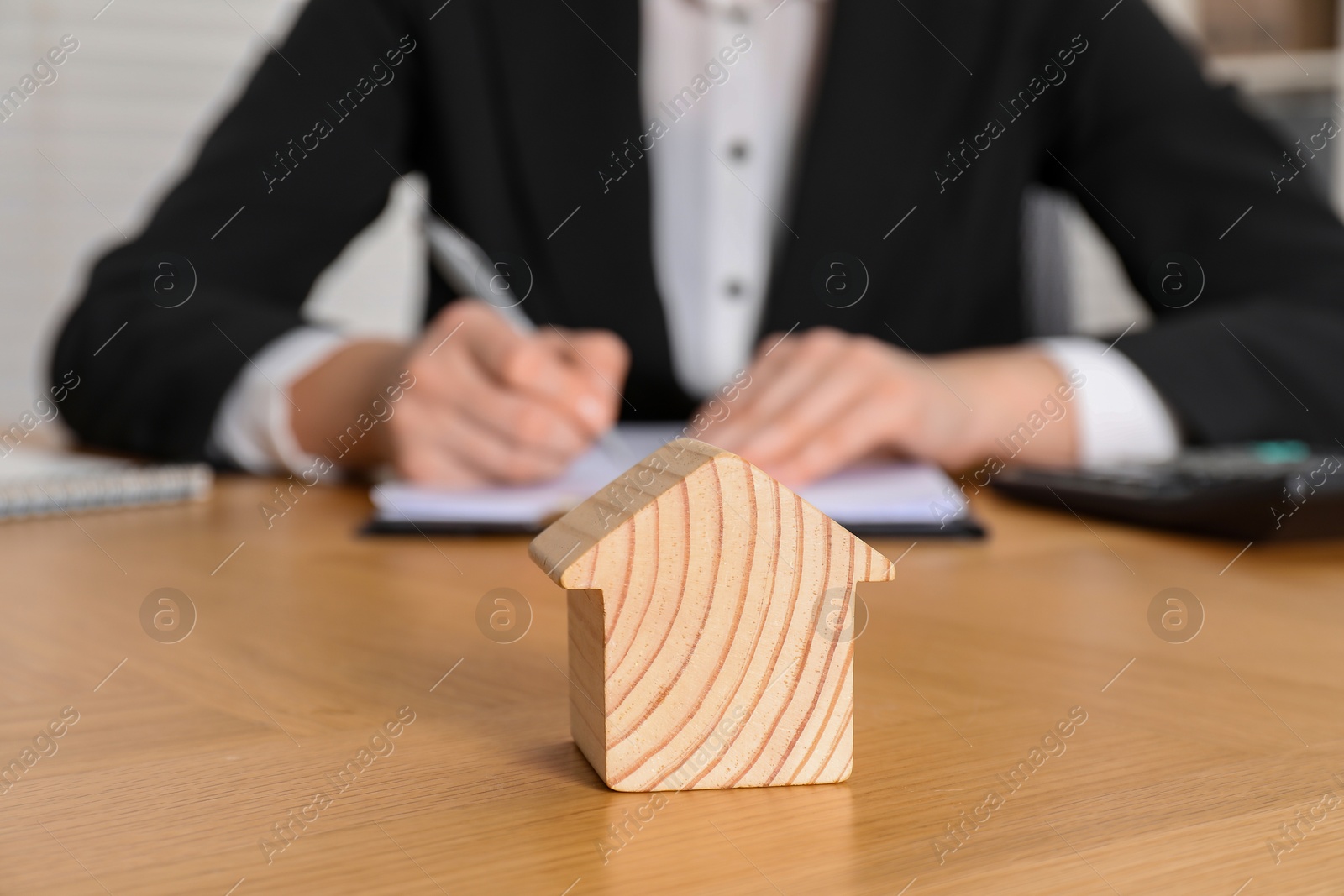 Photo of Property insurance. Real estate agent working at table indoors, focus on wooden house figure