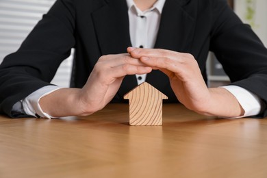 Photo of Property insurance. Real estate agent protecting wooden house figure at table indoors, closeup