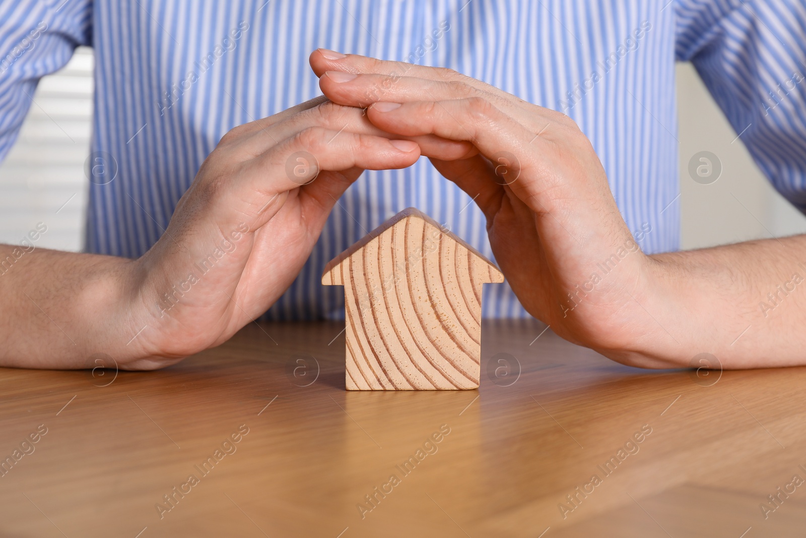 Photo of Property insurance. Real estate agent protecting wooden house figure at table indoors, closeup