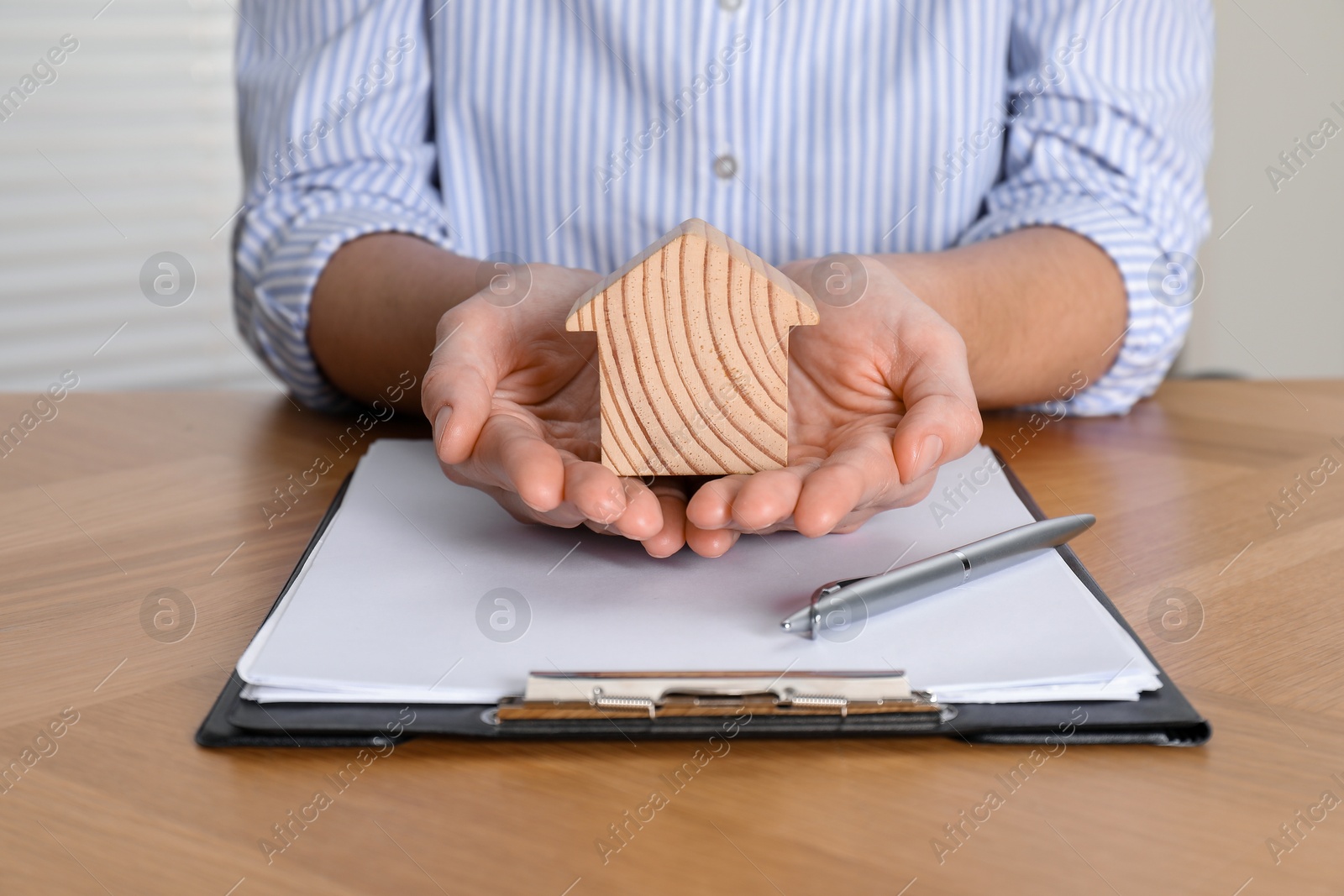 Photo of Property insurance. Real estate agent with wooden house figure at table indoors, closeup