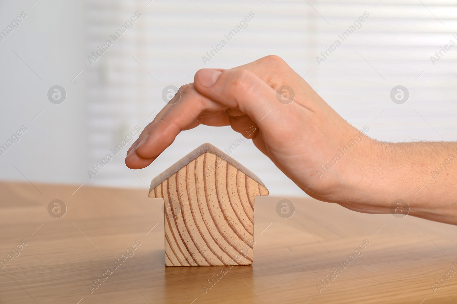 Photo of Property insurance. Real estate agent with wooden house figure at table indoors, closeup