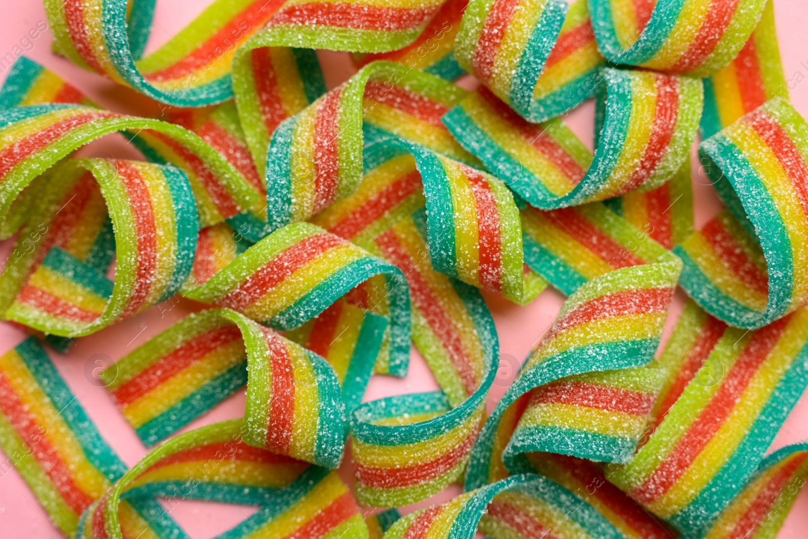 Photo of Tasty rainbow sour belts on pink background, top view