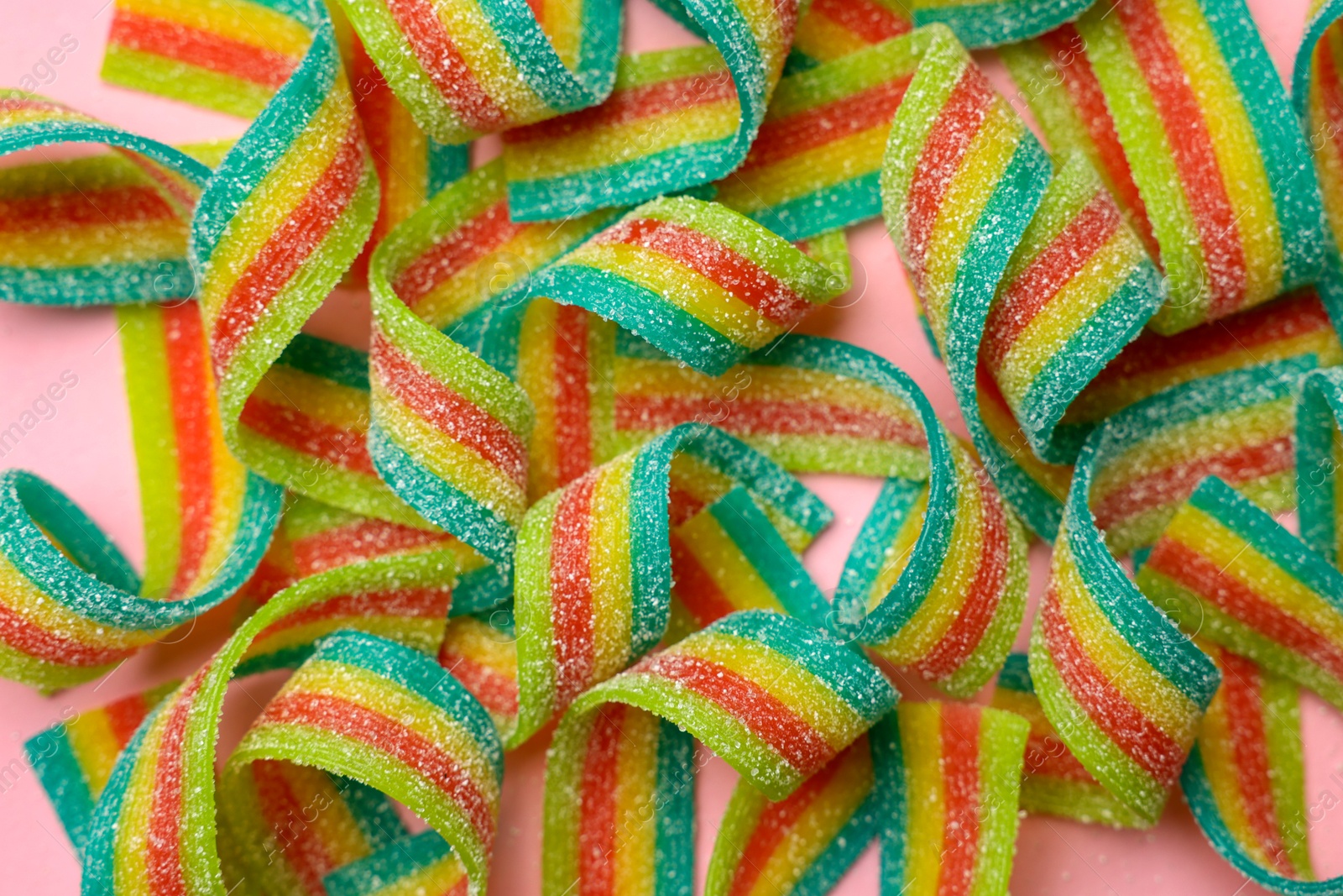 Photo of Tasty rainbow sour belts on pink background, top view