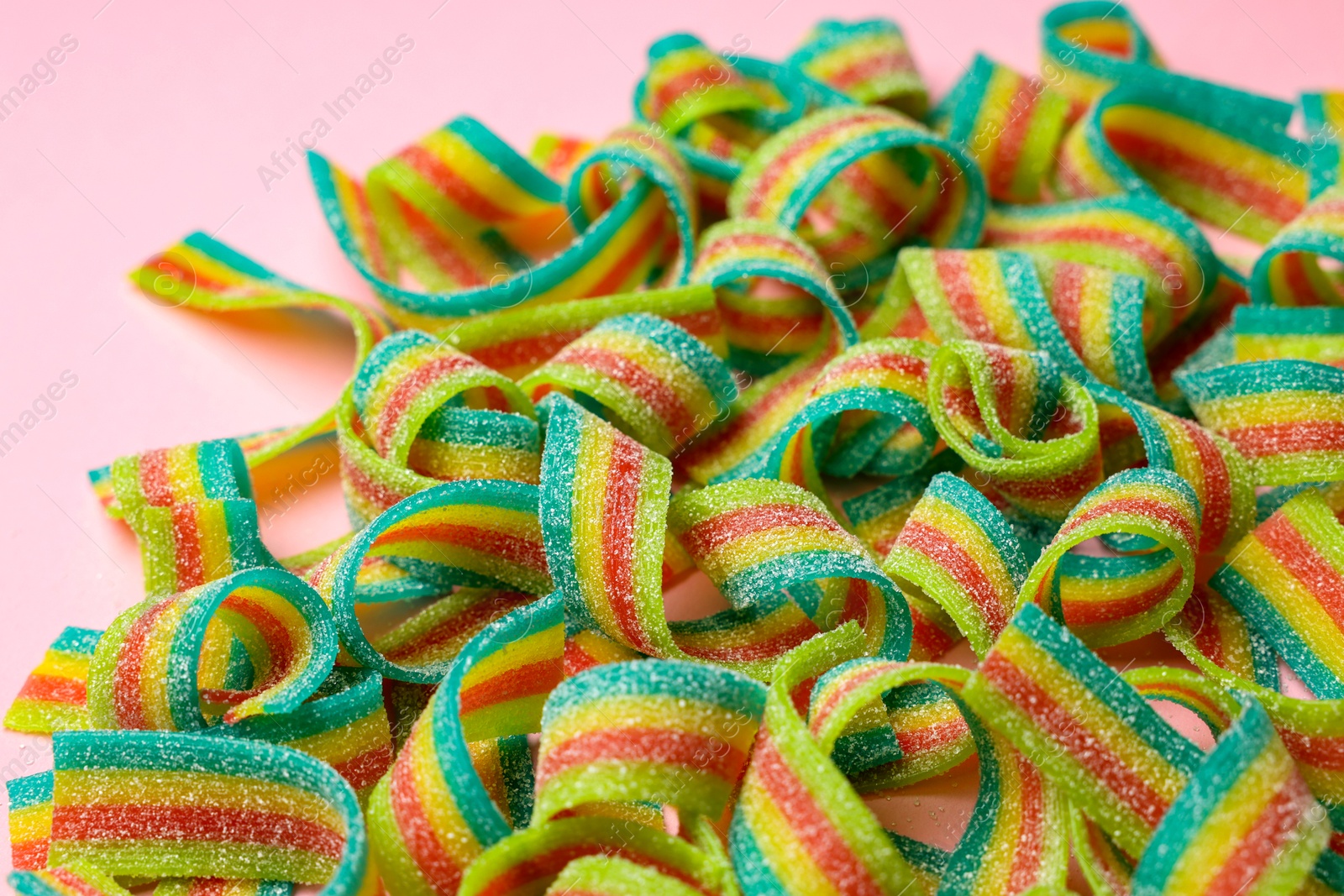 Photo of Tasty rainbow sour belts on pink background, closeup