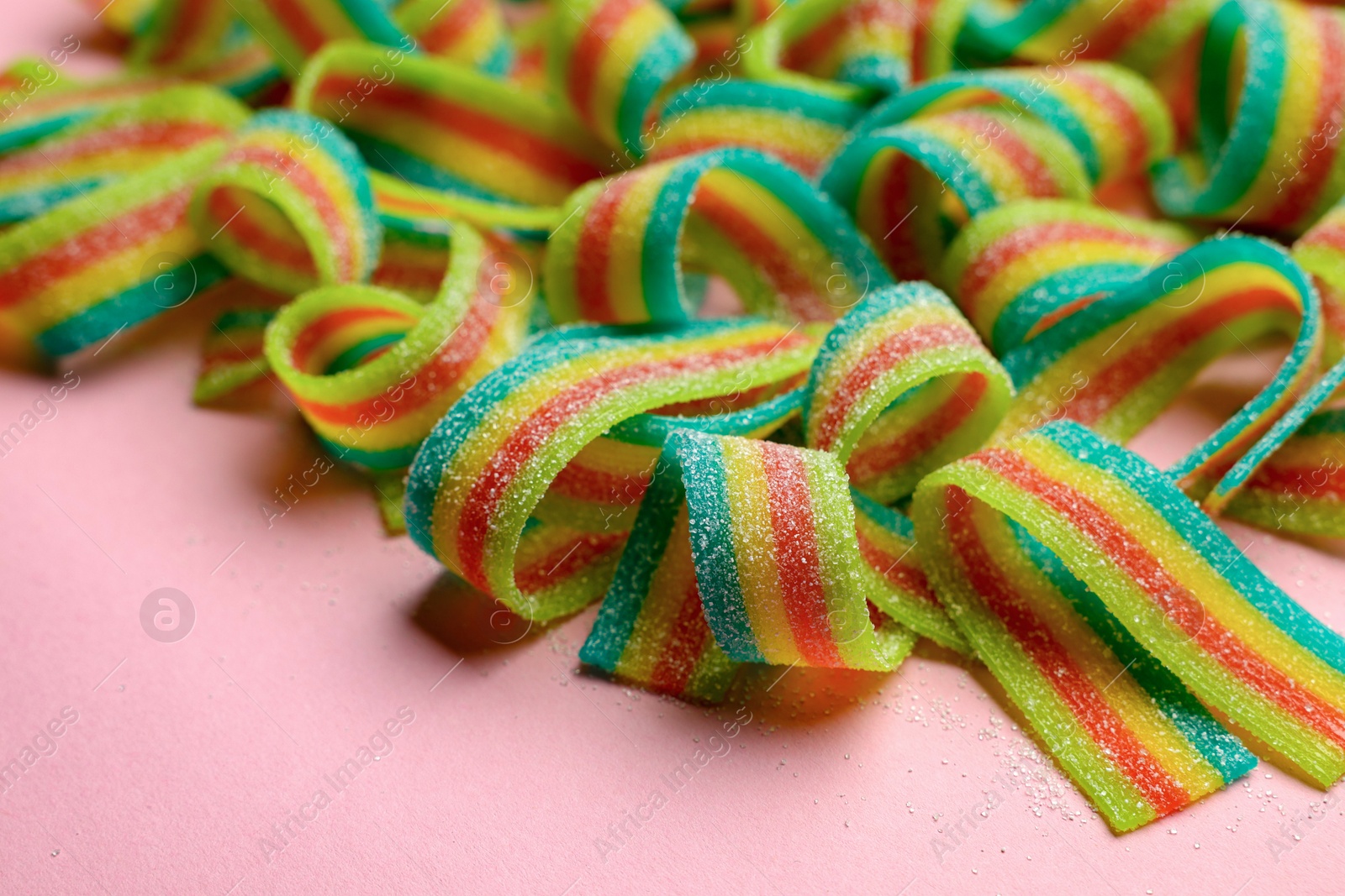 Photo of Tasty rainbow sour belts on pink background, closeup