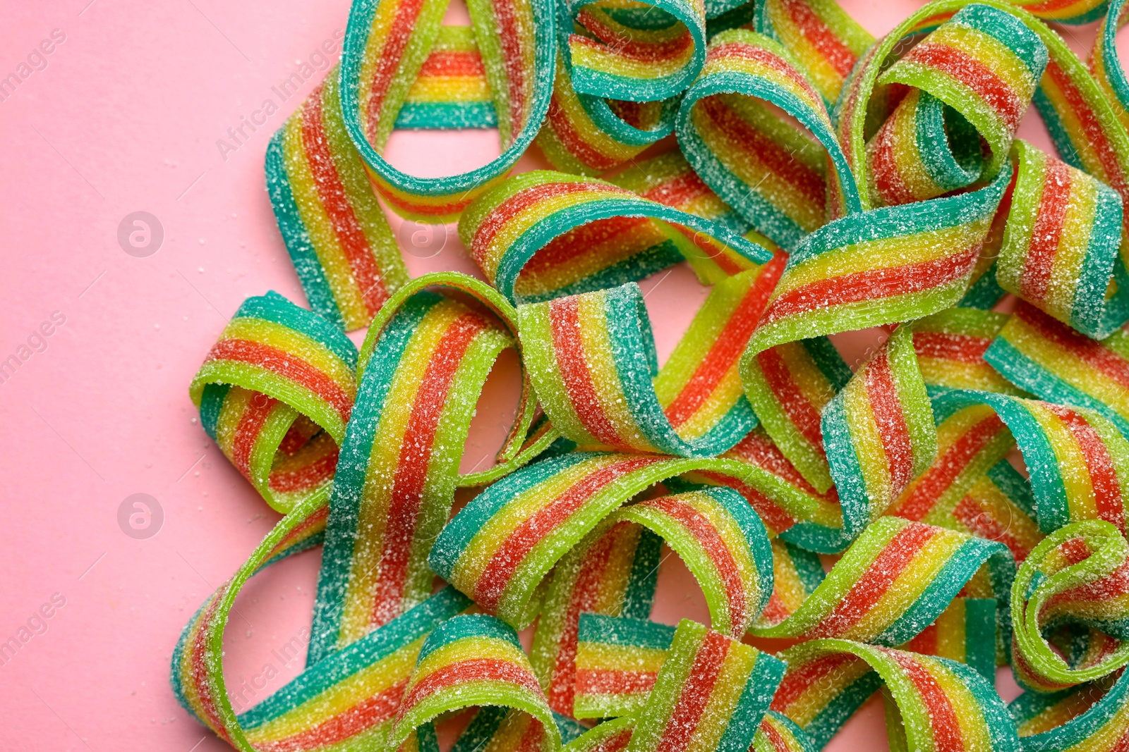 Photo of Tasty rainbow sour belts on pink background, top view