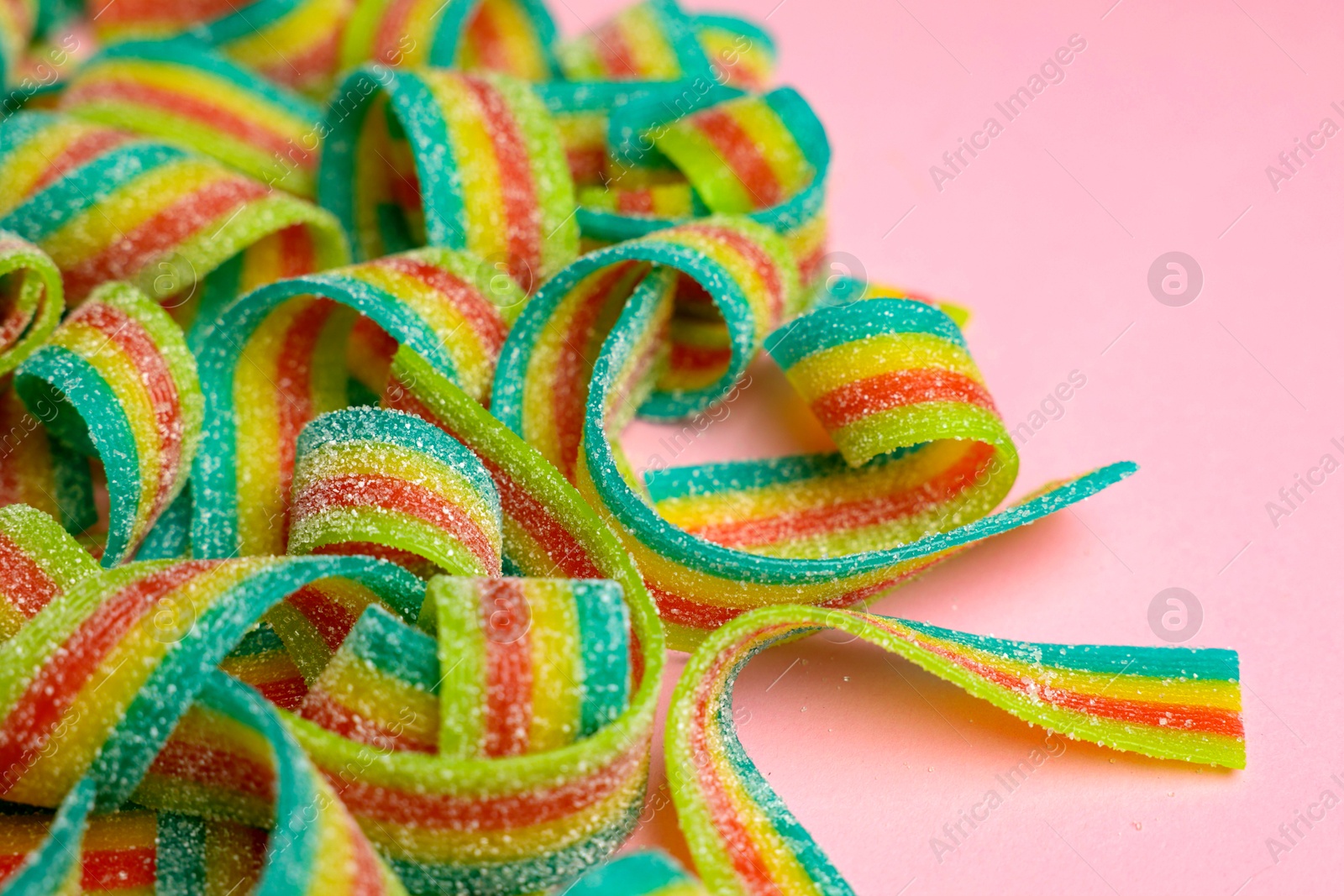 Photo of Tasty rainbow sour belts on pink background, closeup