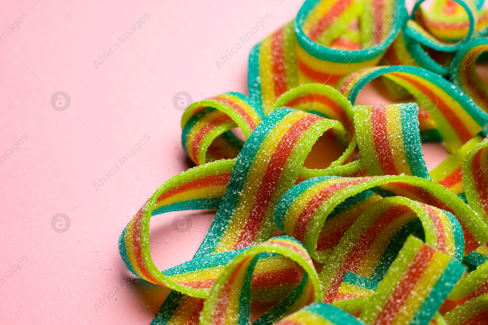 Photo of Tasty rainbow sour belts on pink background, closeup. Space for text