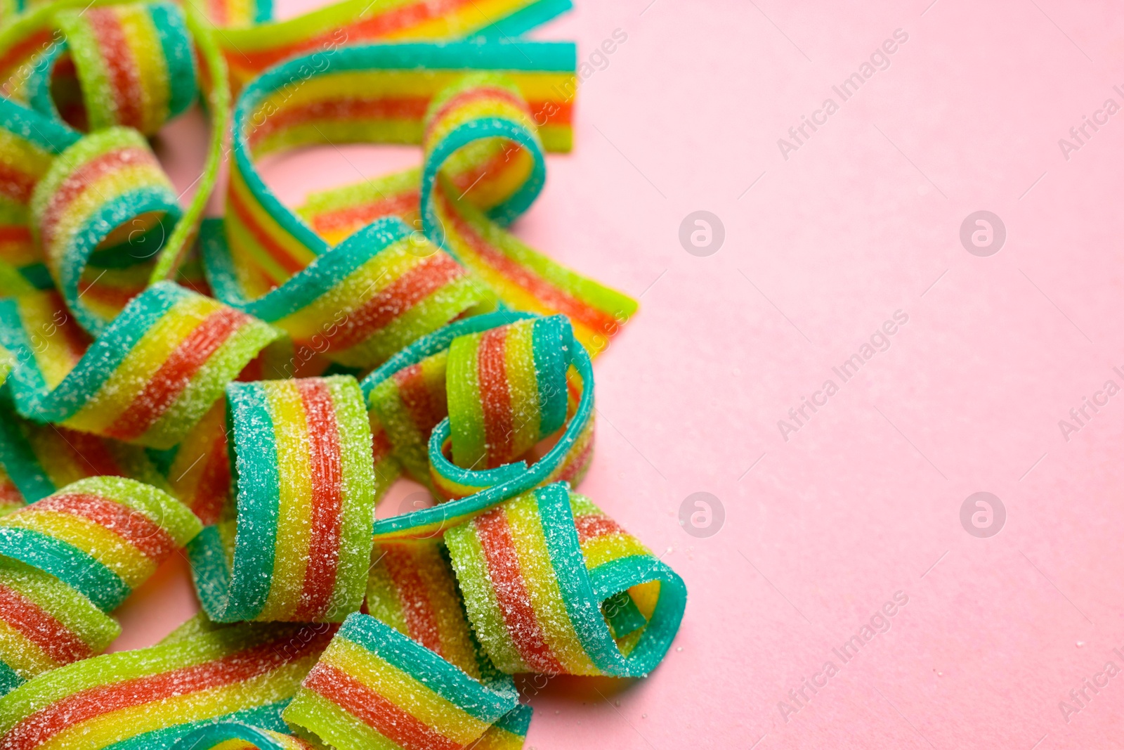 Photo of Tasty rainbow sour belts on pink background, closeup. Space for text