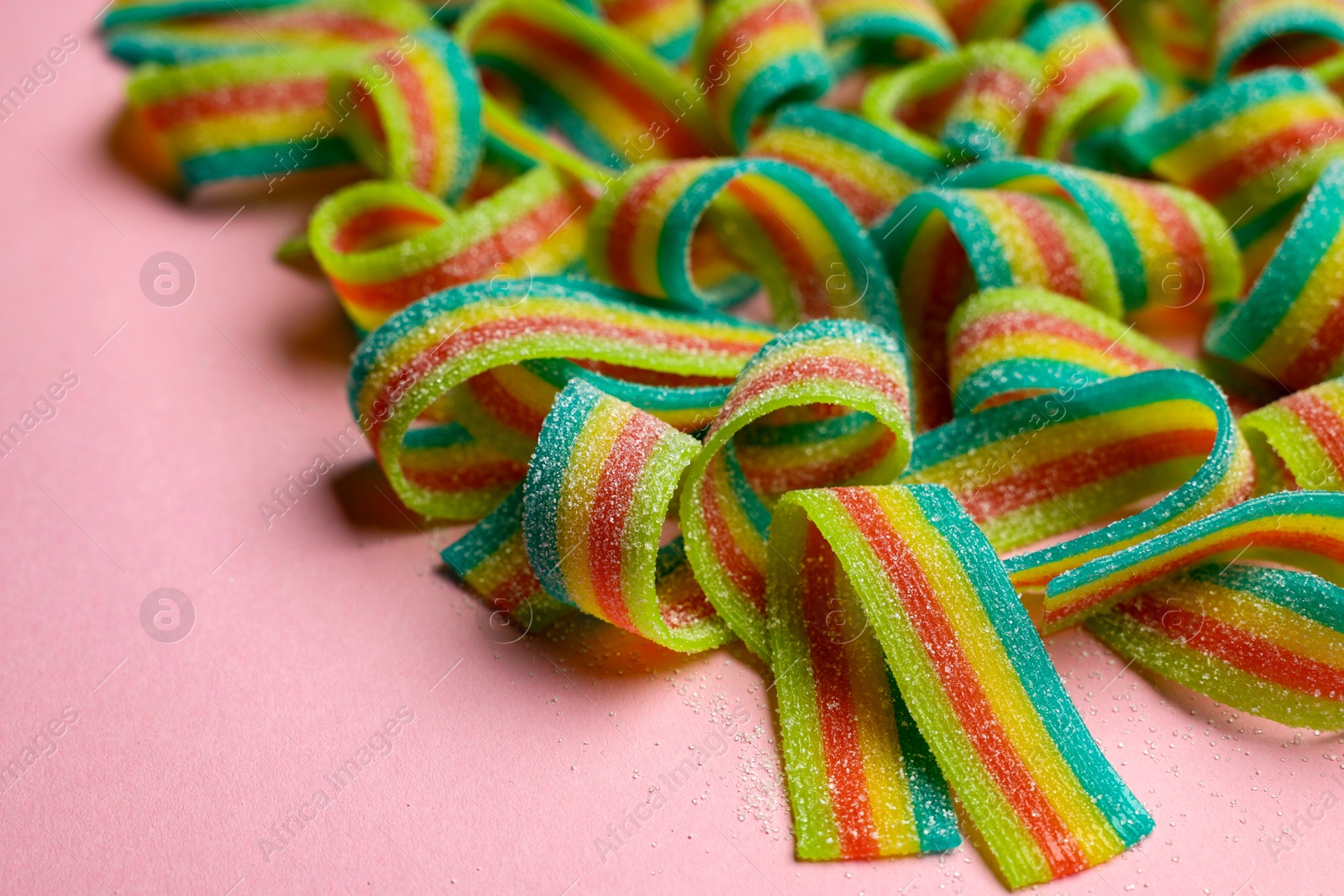 Photo of Tasty rainbow sour belts on pink background, closeup