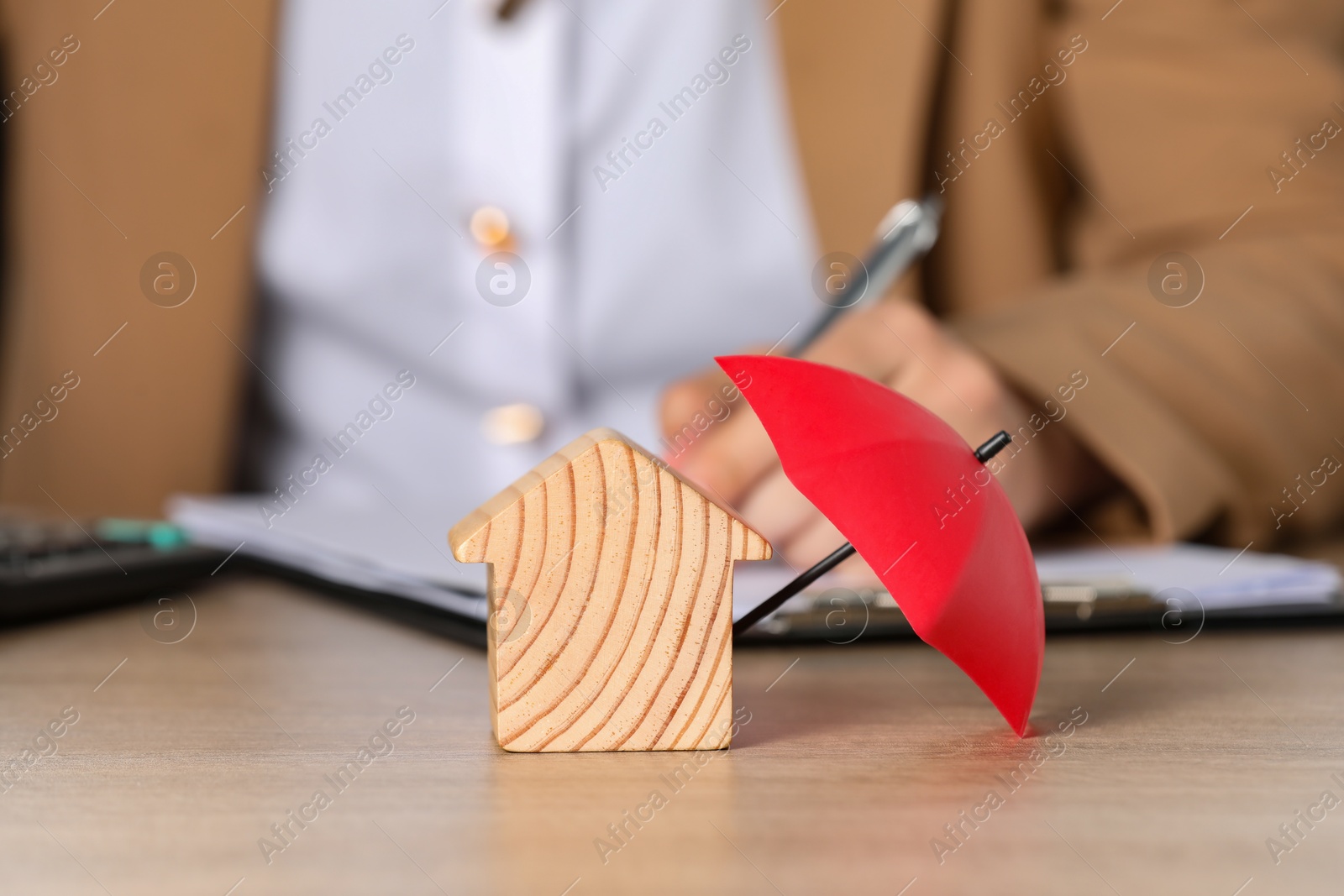 Photo of Property insurance. Real estate agent working at table indoors, focus on wooden house figure and small umbrella