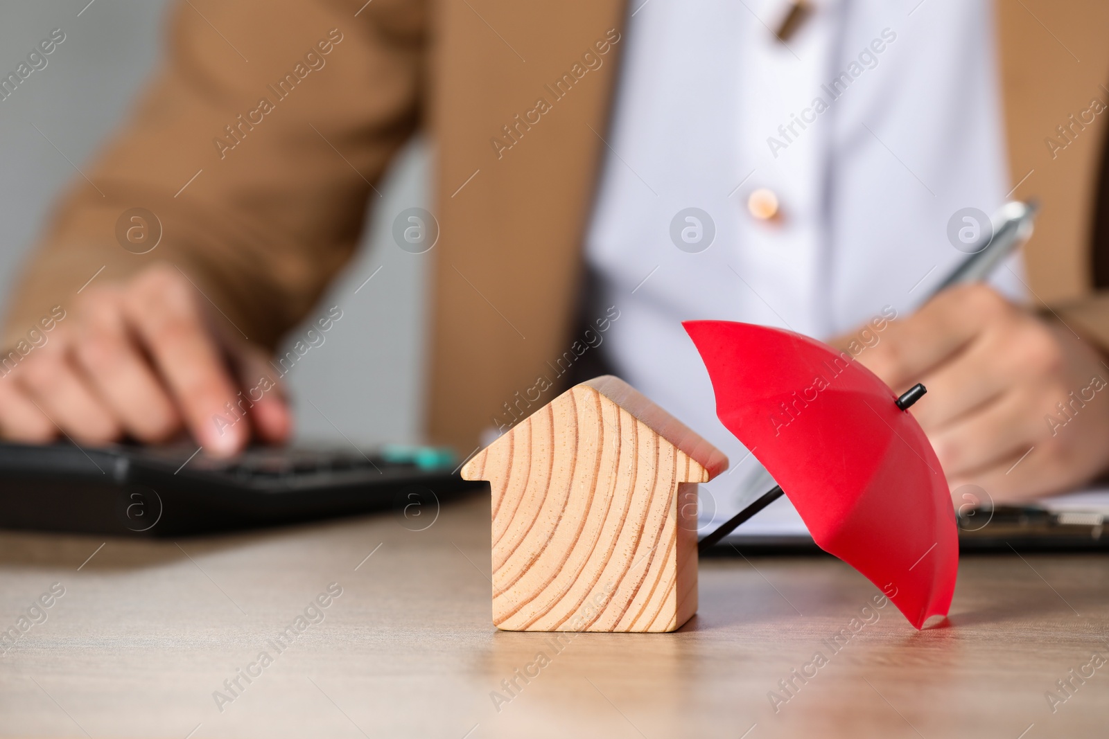 Photo of Property insurance. Real estate agent working at table indoors, focus on wooden house figure and small umbrella