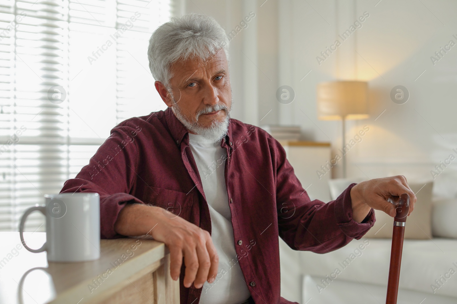 Photo of Lonely senior man with walking cane sitting at table in room