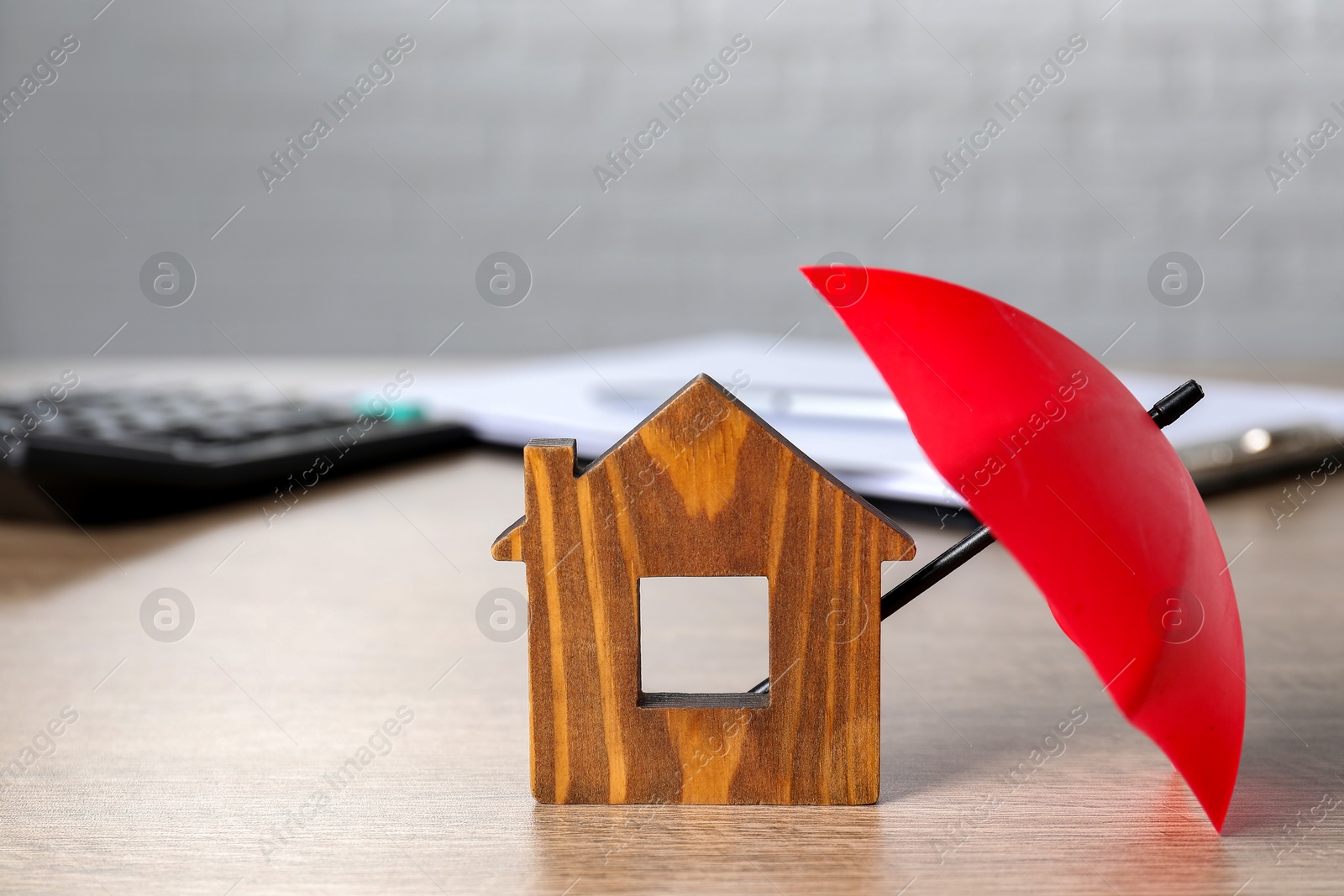 Photo of Property insurance. Wooden house figure and small umbrella on table indoors