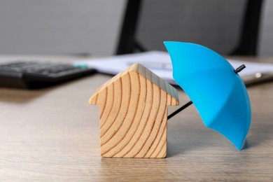 Photo of Property insurance. Wooden house figure and small umbrella on table indoors