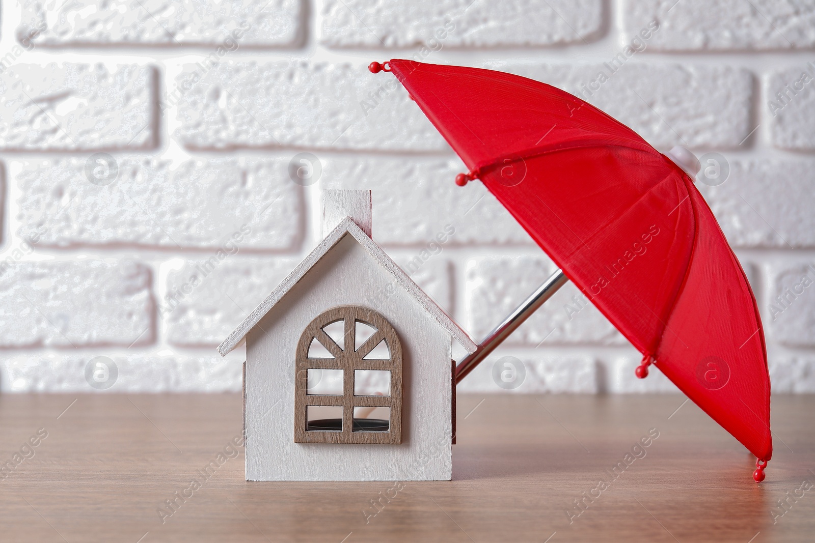 Photo of Property insurance. House figure and small umbrella on table indoors