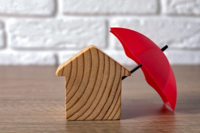 Photo of Property insurance. Wooden house figure and small umbrella on table indoors