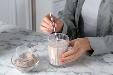 Photo of Woman with glass of protein cocktail at white marble table, closeup