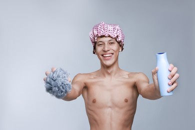 Photo of Man in shower cap, mesh sponge and shampoo on grey background