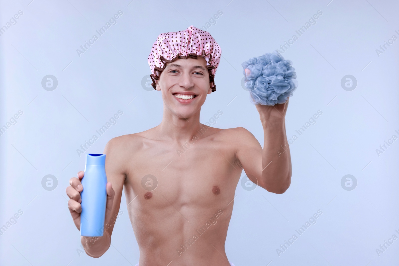 Photo of Man with shower cap, mesh sponge and shampoo on light grey background