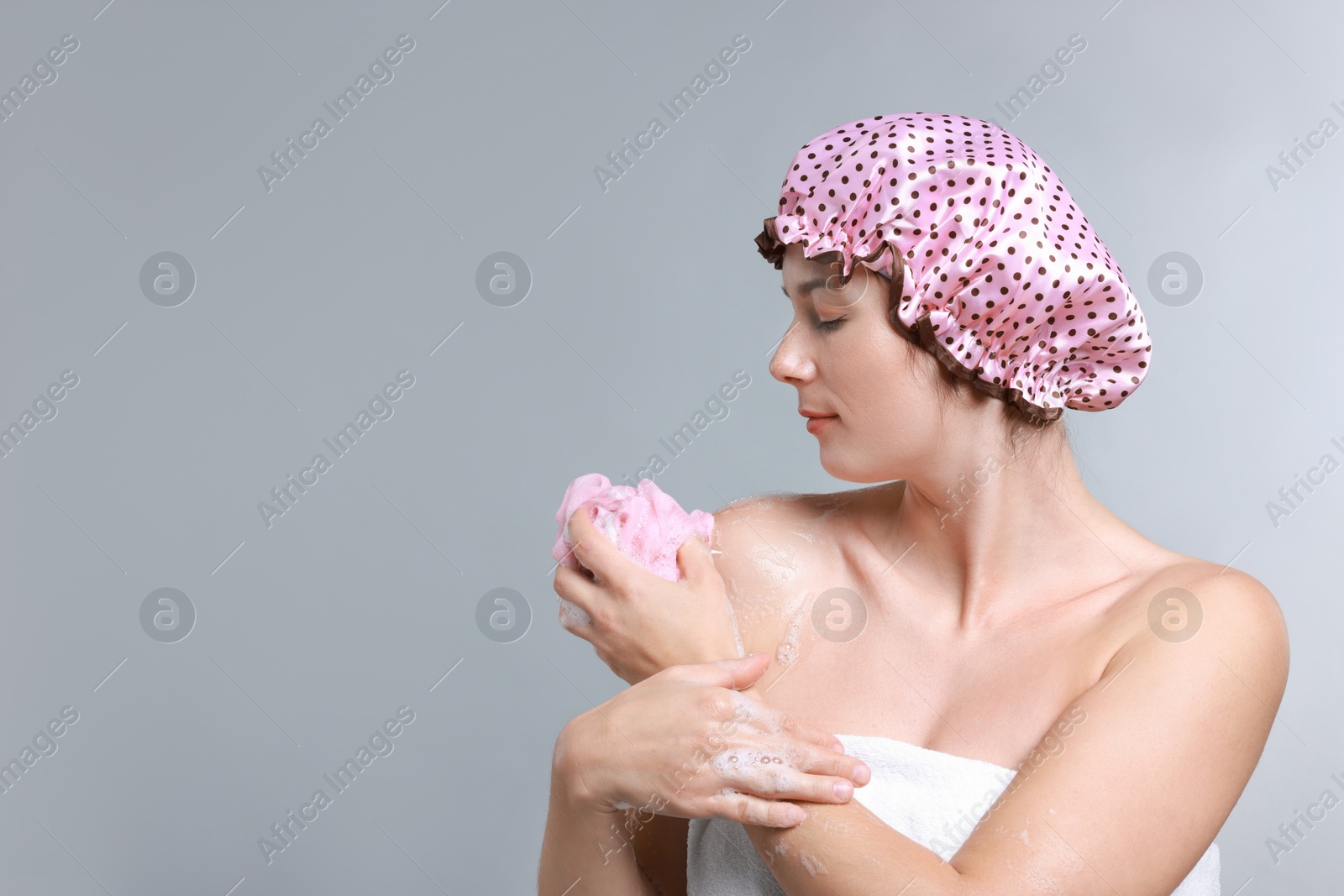 Photo of Woman with shower cap and mesh sponge on grey background, space for text