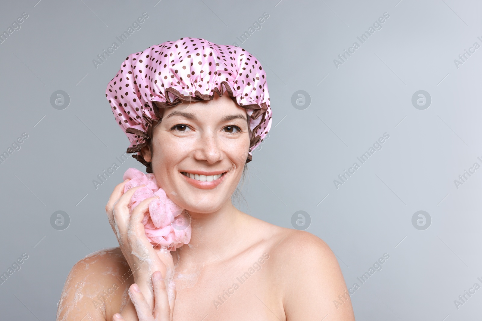 Photo of Woman with shower cap and mesh sponge on grey background