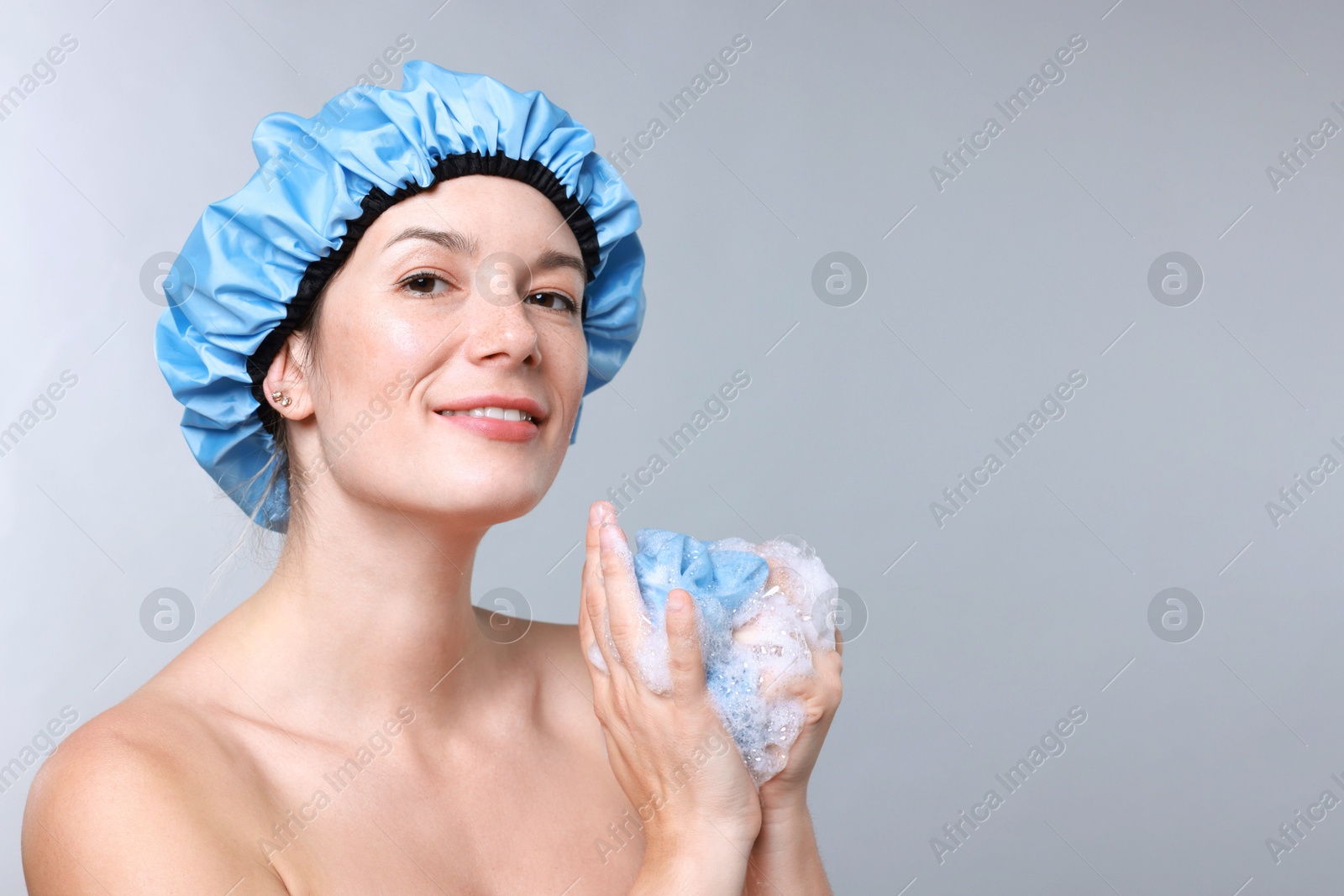 Photo of Woman with shower cap and mesh sponge on grey background, space for text