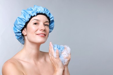 Photo of Woman with shower cap and mesh sponge on grey background, space for text