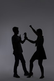 Photo of Domestic violence. Silhouette of woman with high-heeled shoe threatening her husband on grey background