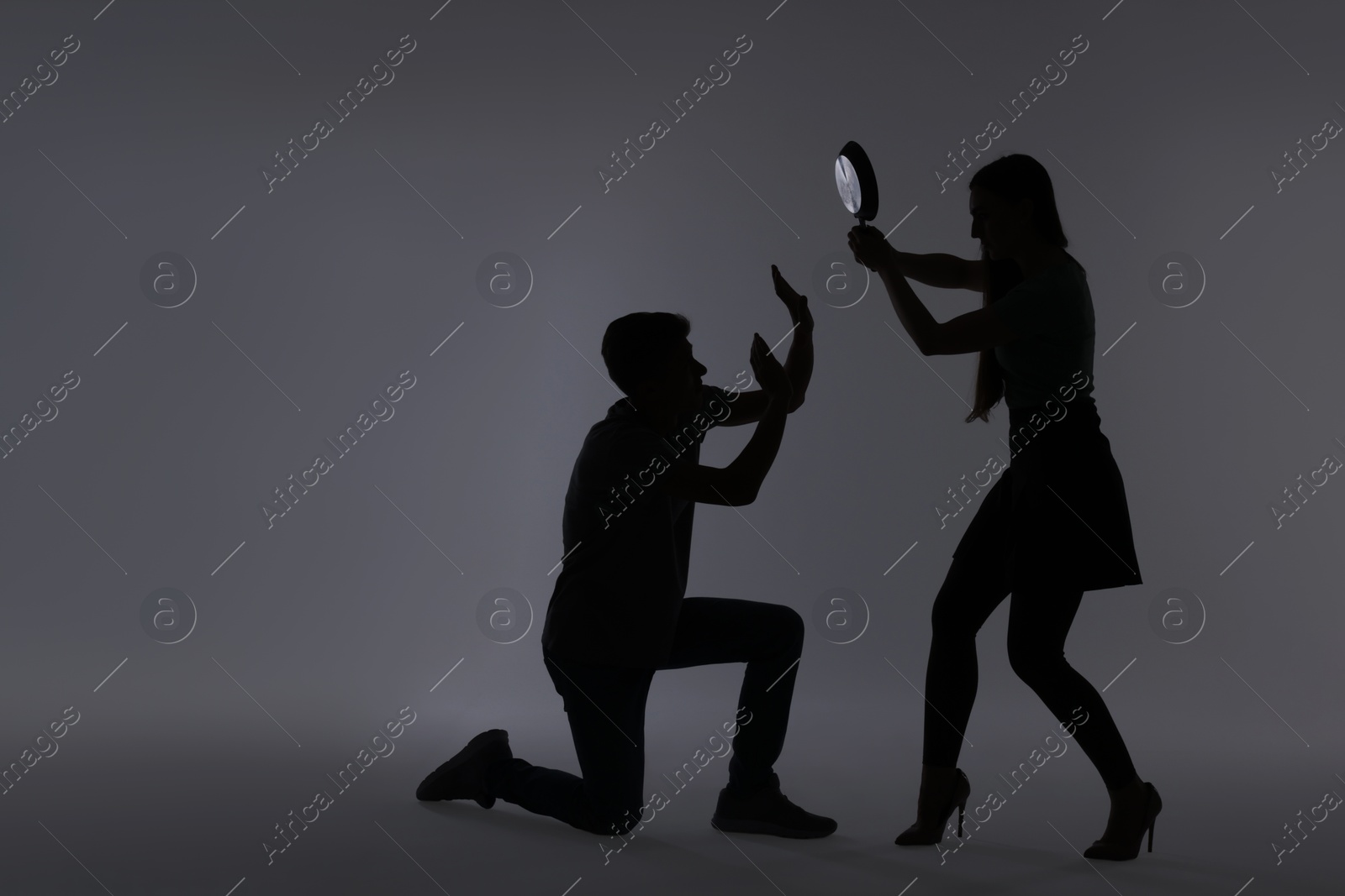 Photo of Domestic violence. Silhouette of woman with frying pan threatening her husband on grey background