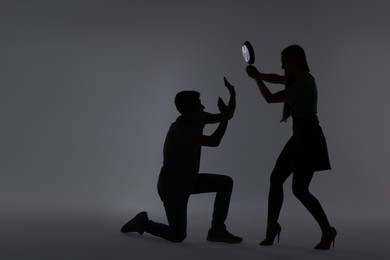 Photo of Domestic violence. Silhouette of woman with frying pan threatening her husband on grey background