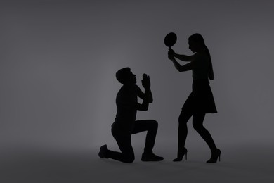 Photo of Domestic violence. Silhouette of woman with frying pan threatening her husband on grey background